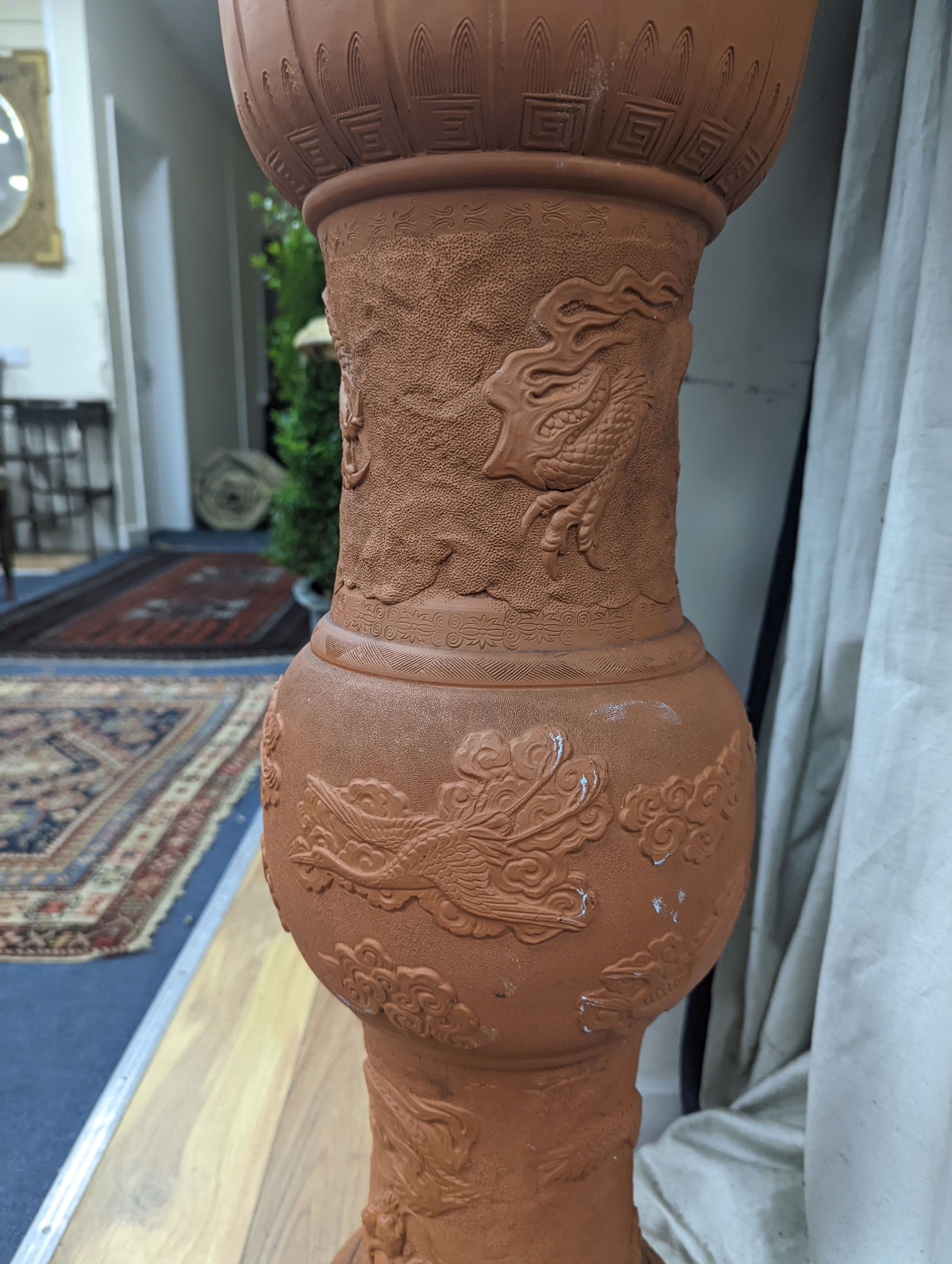 A Chinese earthenware jardiniere on stand moulded with dragons. Height 99 cms.